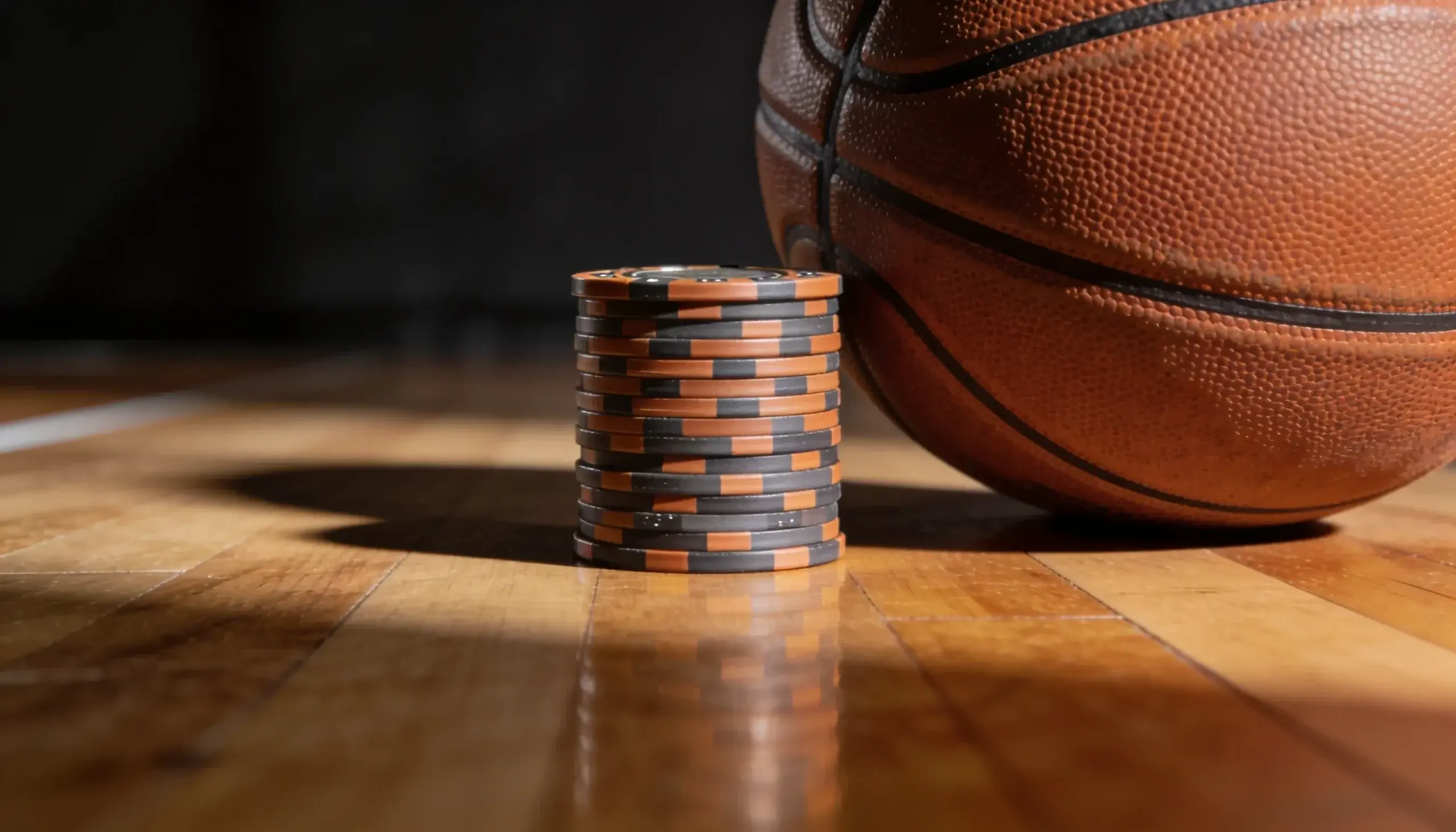 Stacked betting chips beside a basketball on a polished hardwood floor